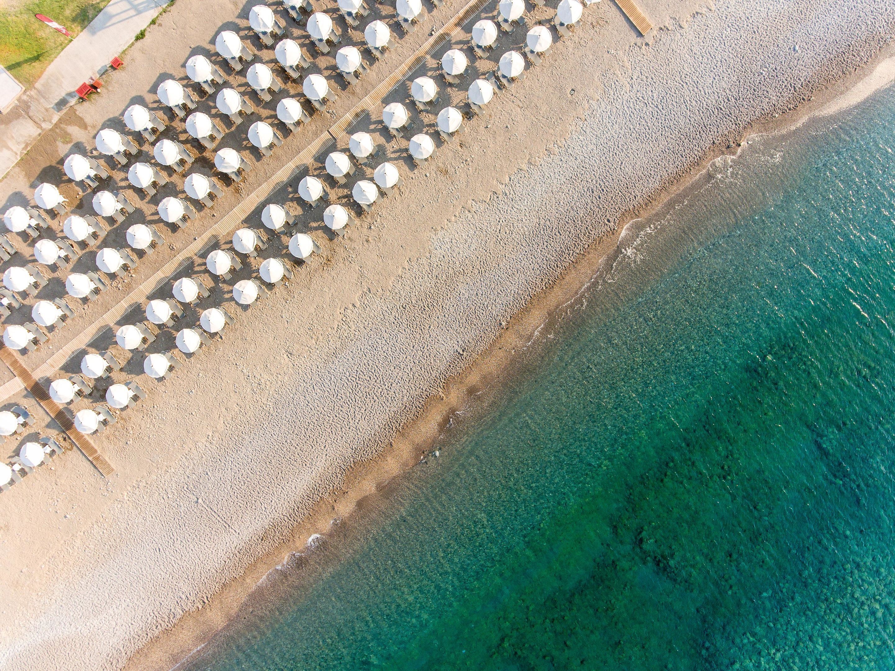 Vue aérienne d’une plage où l’on aperçoit des rangées de parasols blancs et de chaises longues.