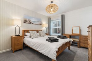 Ein ordentlich eingerichtetes Schlafzimmer mit Bett, Nachttischen, Kommode und einem Bild an der Wand.