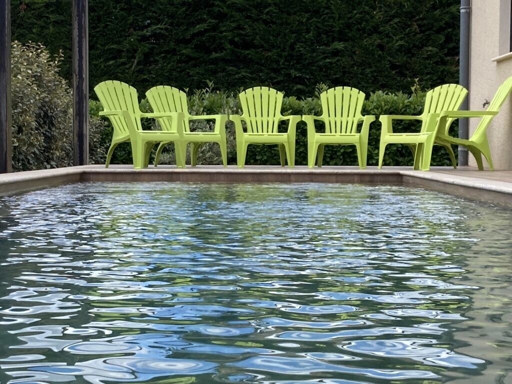 A pool with clear water and green chairs along the edge.