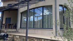 Ein modernes Haus mit Steinfundament, großen Fenstern und einer überdachten Terrasse.
