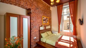 Un dormitorio con pared de ladrillo, estructura de cama de madera y ventana con cortinas.