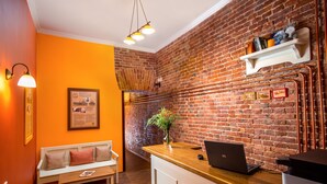 Un interior moderno con pared de ladrillo, un mostrador de recepción de madera, un banco blanco y una pequeña planta.