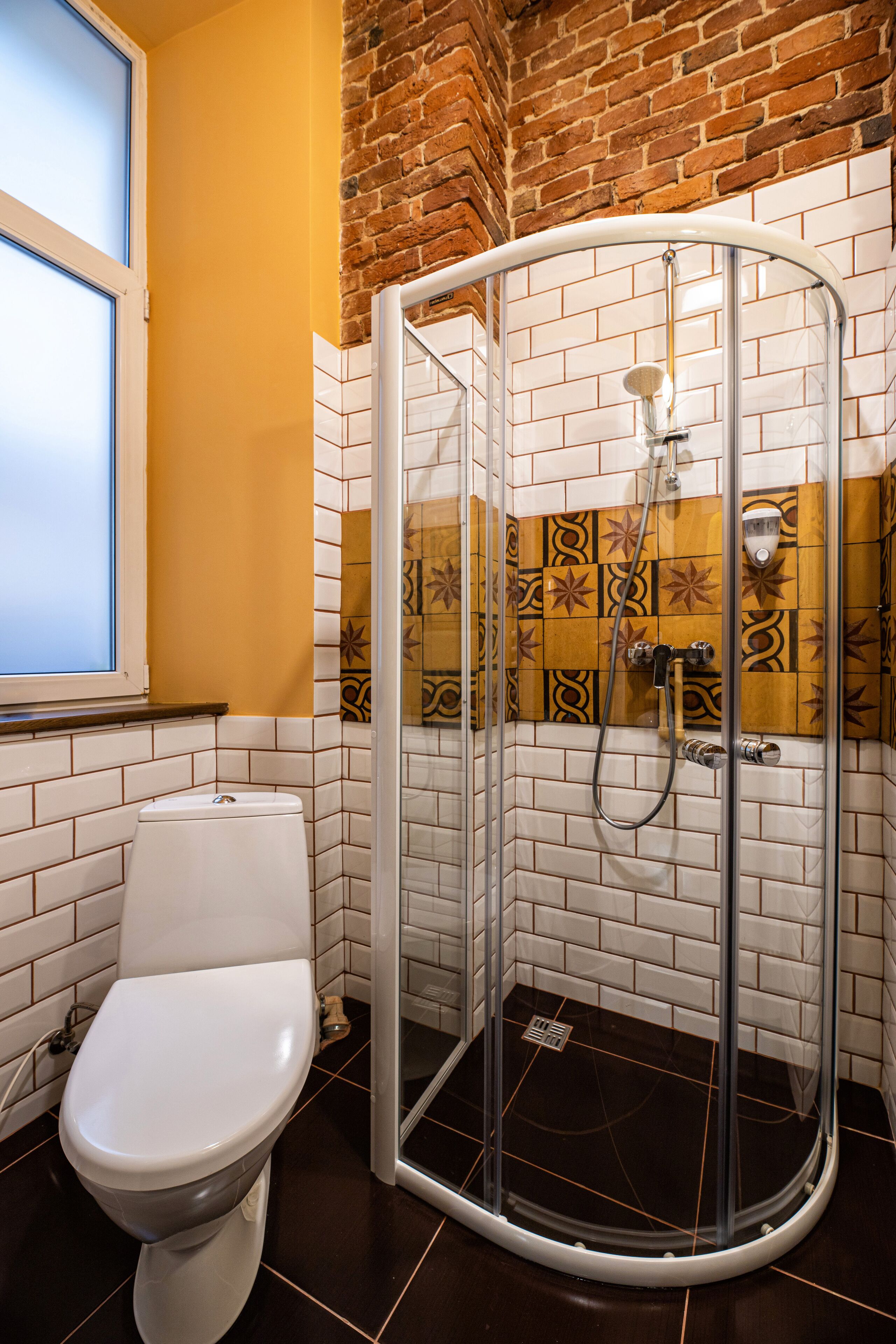 Een badkamer met een wit toilet, een douchecabine van glas en een geel bakstenen muur.