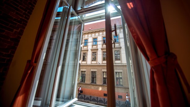 Vista a través de una ventana con cortinas, mostrando un edificio con varias ventanas y balcones.