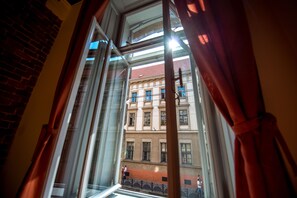 A view through a window with curtains, revealing a building with multiple windows and balconies. - Post House Rooms (Lviv)