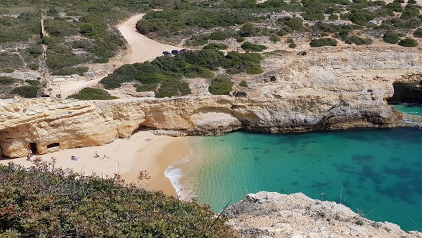 Un paysage côtier caractérisé par une plage de sable, des eaux turquoise et limpides, et des falaises rocheuses.