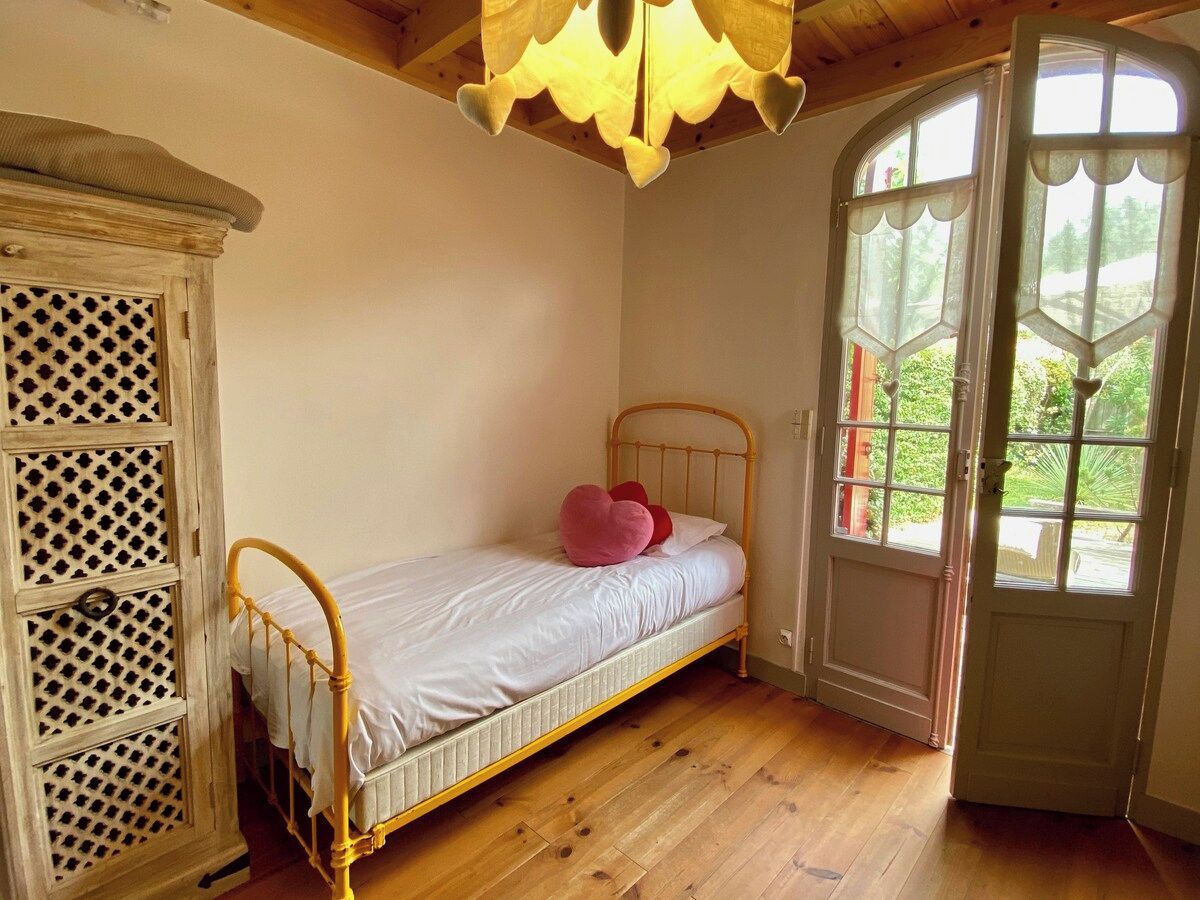 A bedroom with a single bed, a wooden wardrobe, and a window with a view of greenery.
