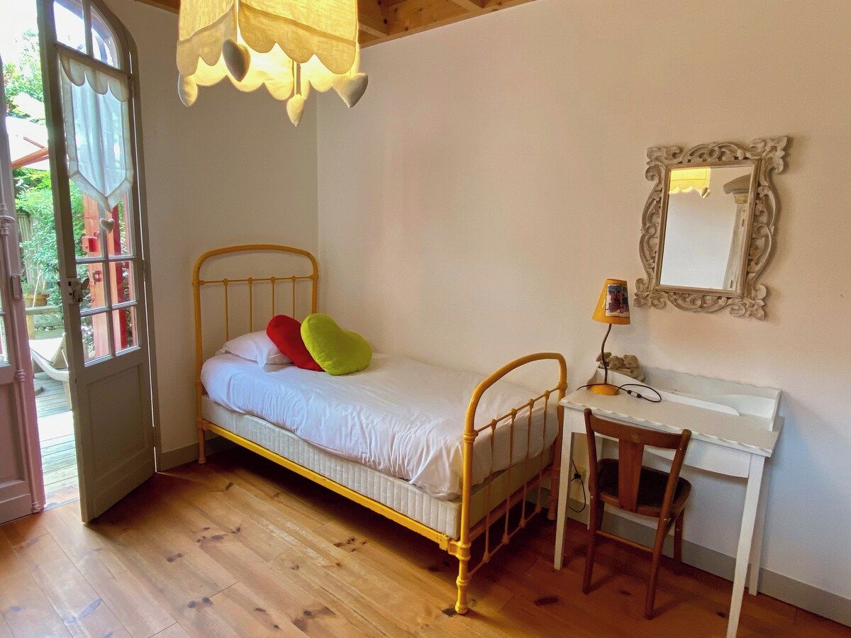 A single bed with a headboard, a desk with a chair, and a mirror on the wall.