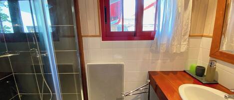 Ein Badezimmer mit Dusche, einem Fenster mit rotem Rahmen, einem Handtuchhalter und einem Waschbecken mit Spiegel.