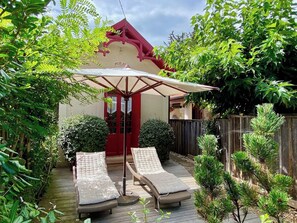 Un patio con dos sillones de descanso y una mesa bajo un toldo, rodeado de follaje y una valla de madera.