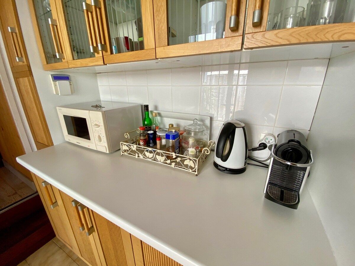 A kitchen with a microwave, a coffee maker, a kettle, and a spice rack.
