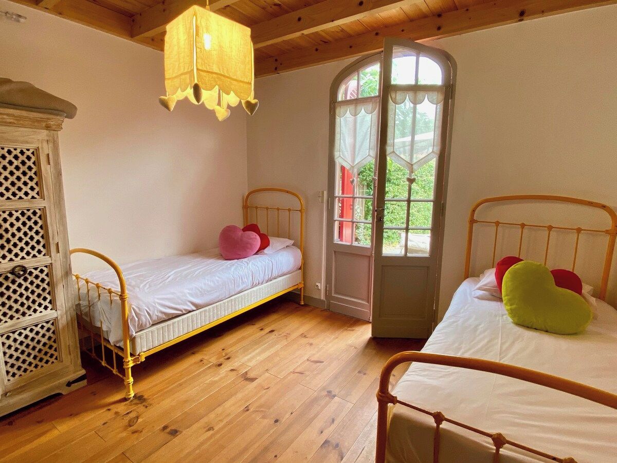 Une chambre avec deux lits, un plancher en bois, une armoire blanche et une fenêtre donnant sur un paysage verdoyant.