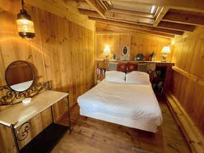 A wooden room with a bed, a bedside table, a mirror, and two wall-mounted lamps. - Idyllic chalet near the beach in Cap Ferret A0337 (Lège-Cap-Ferret)