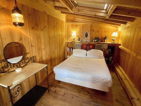 Una habitación de madera con una cama, una mesita de noche, un espejo y dos lámparas de pared.