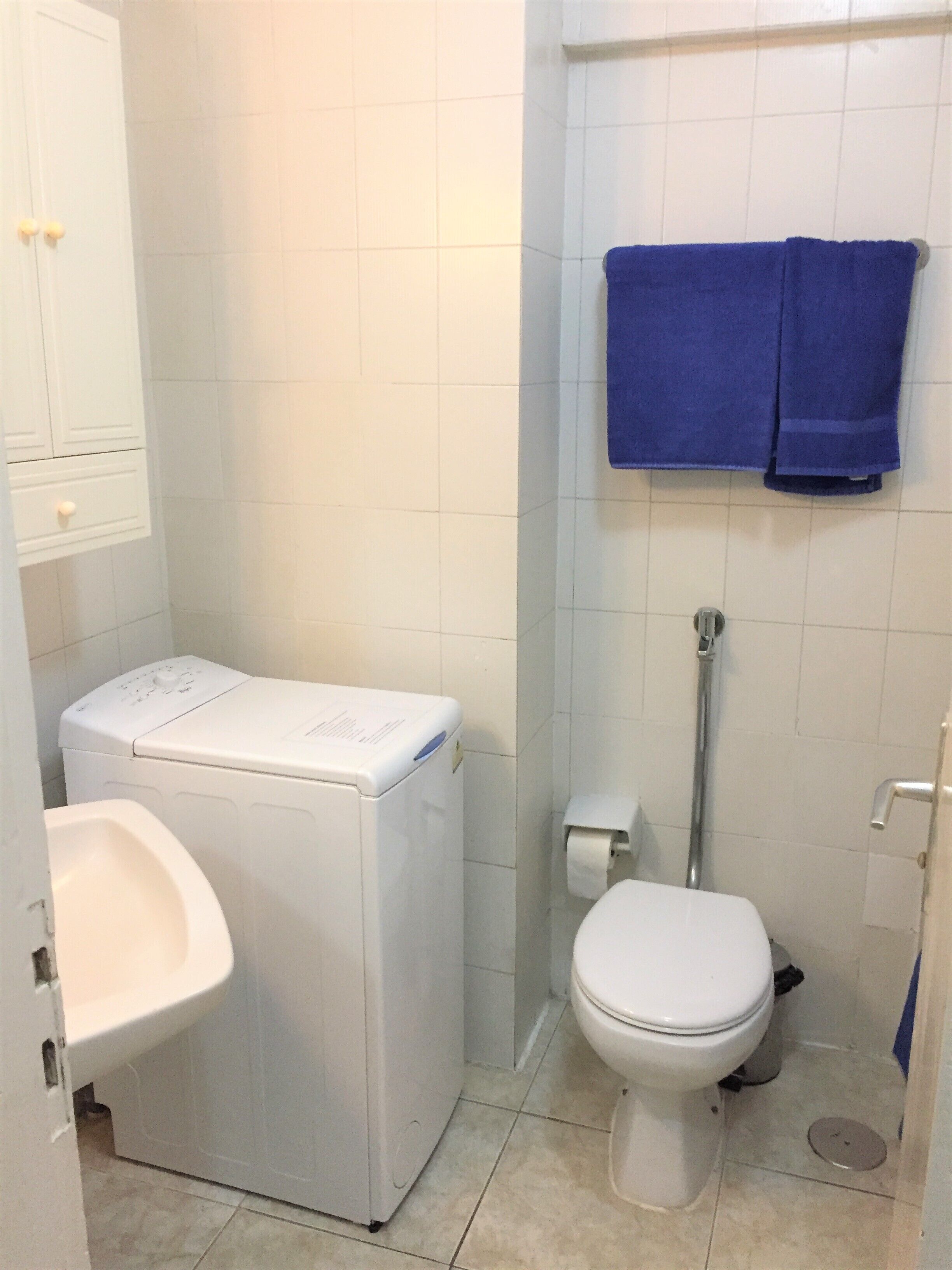 Un baño pequeño con lavadora blanca, inodoro y lavabo.