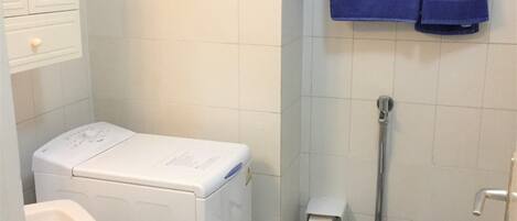 Un baño pequeño con lavadora blanca, inodoro y lavabo.