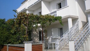 A white multi-story building with a staircase leading to the entrance, a small outdoor seating area, and a tree with green leaves in front. - Apartment in Kampor with Seaview, Terrace, Air condition, WIFI (4610-2) (Kampor)