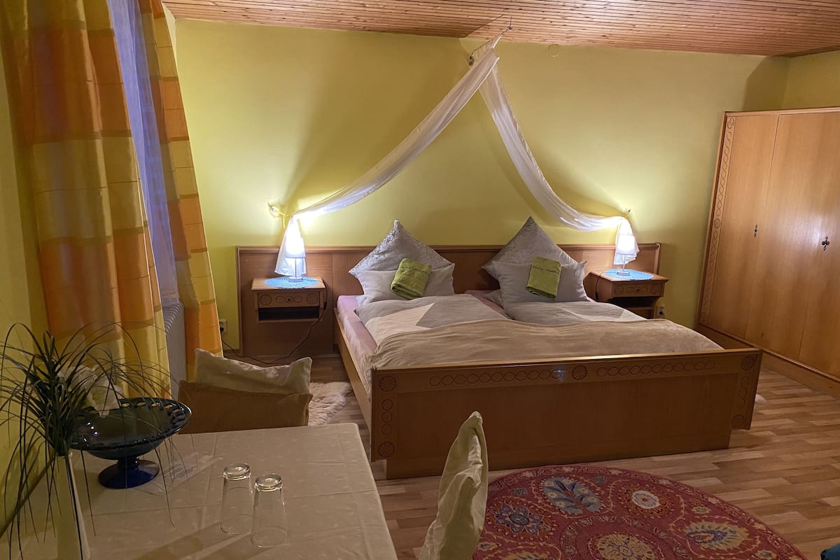 A bedroom with a four-poster bed, bedside tables with lamps, a small table with glasses, and a decorative rug.