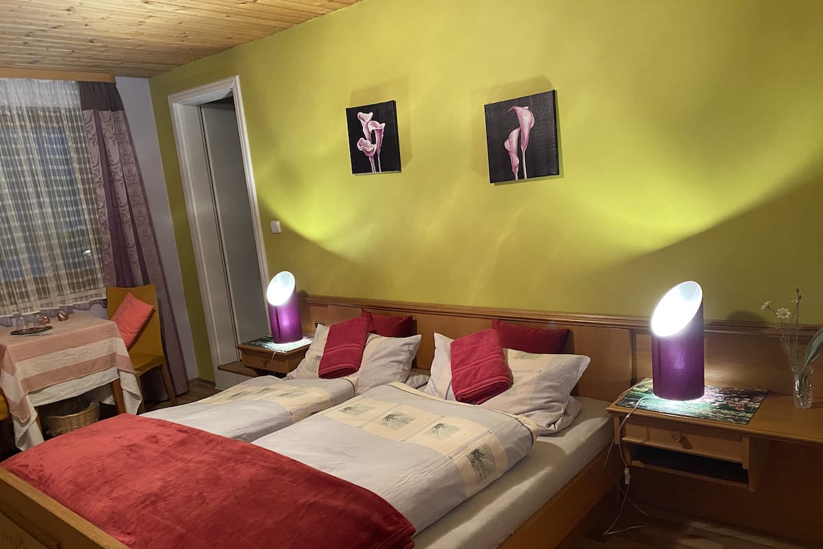 A double bed with red and white bedding, two wall-mounted lamps, and two paintings on the wall.