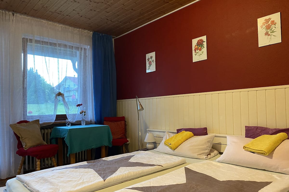 A bedroom with a bed, a table with a vase of flowers, and a window with curtains.