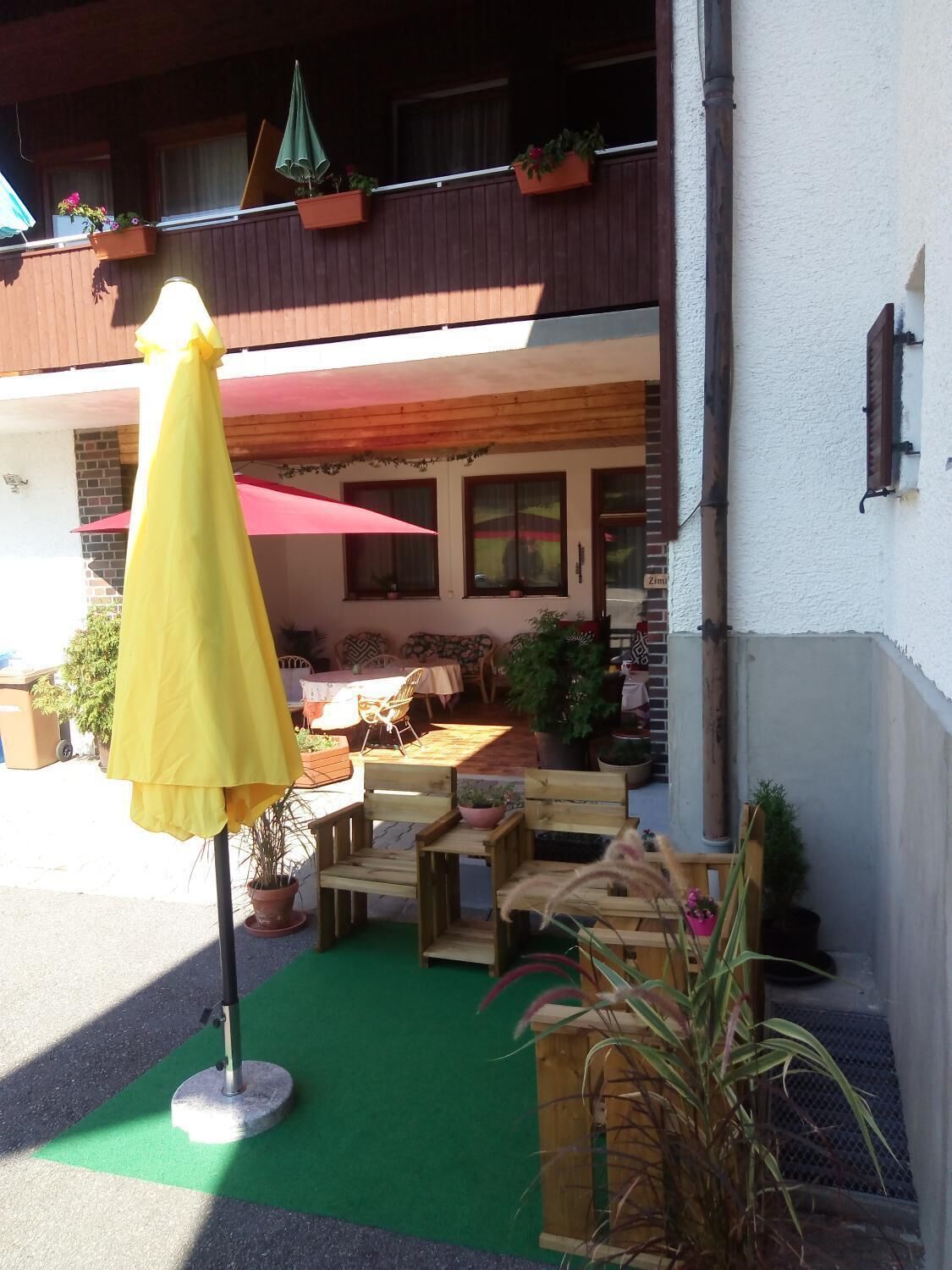 An outdoor seating area with wooden tables and chairs, a yellow umbrella, and potted plants.
