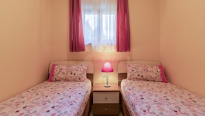 Een slaapkamer met twee eenpersoonsbedden, een nachtkastje met een lamp en een raam met gordijnen.