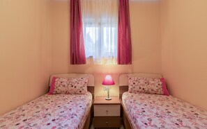 A bedroom with two single beds, a nightstand with a lamp, and a window with curtains.