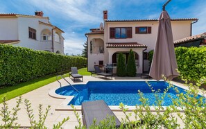 Ein privater Poolbereich mit Liege, Grill und einer Pergola mit Sonnenschirm.