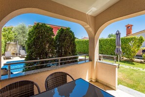 Ein überdachter Außenbereich mit Pool, Sitzgelegenheiten und Blick auf ein Gebäude und Bäume.
