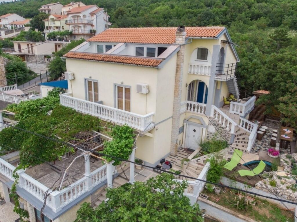 Une maison à deux étages avec un balcon, un petit jardin et un escalier menant à l’étage supérieur.