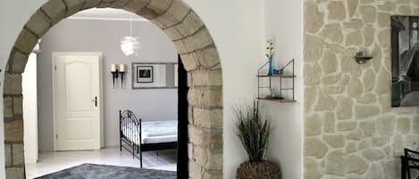 A living room with a stone wall, a brown leather sofa, a small wooden stool, and a black metal gate leading to a bedroom.