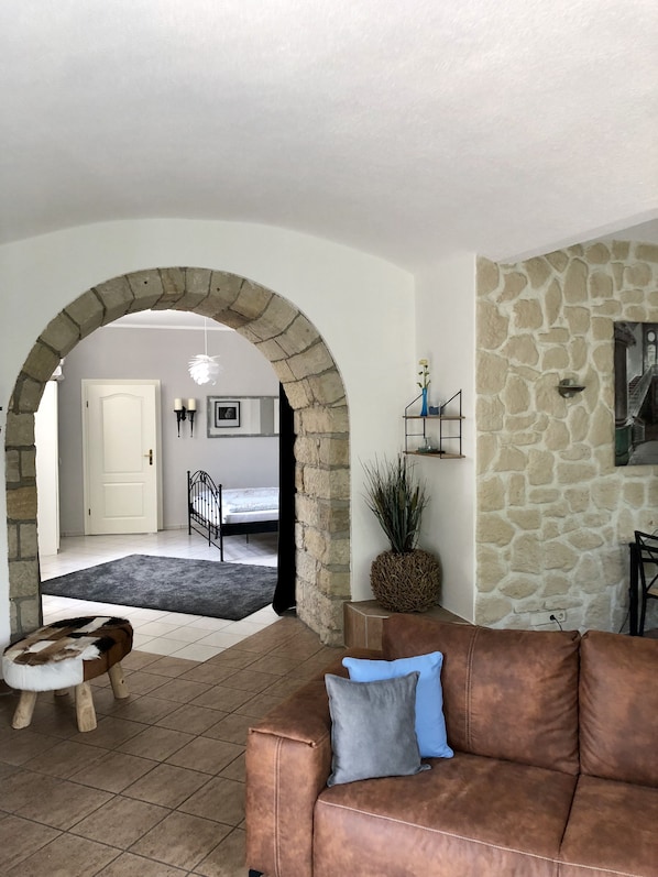 A living room with a stone wall, a brown leather sofa, a small wooden stool, and a black metal gate leading to a bedroom. - Vacation apartment in the Villa Graf von Pfeil on the banks of the Elbe (Neustadt)