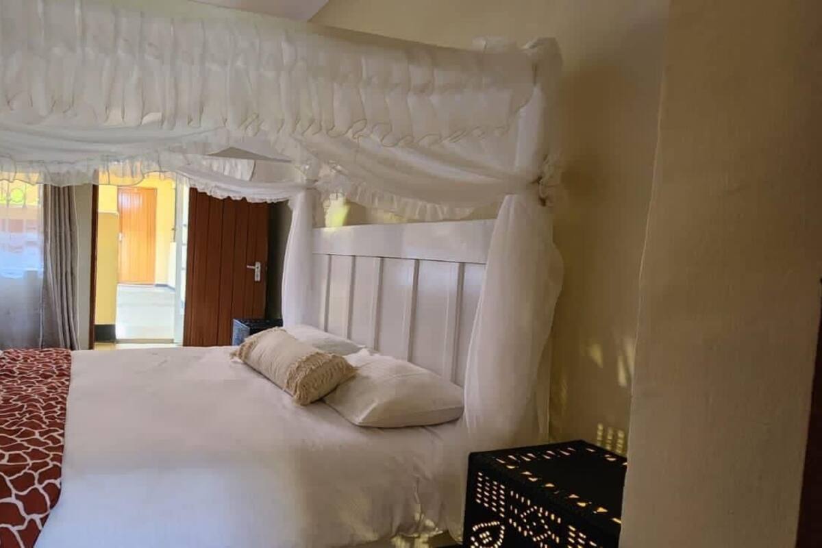 Een slaapkamer met hemelbed, uitzicht op buiten en een deur naar een andere kamer.