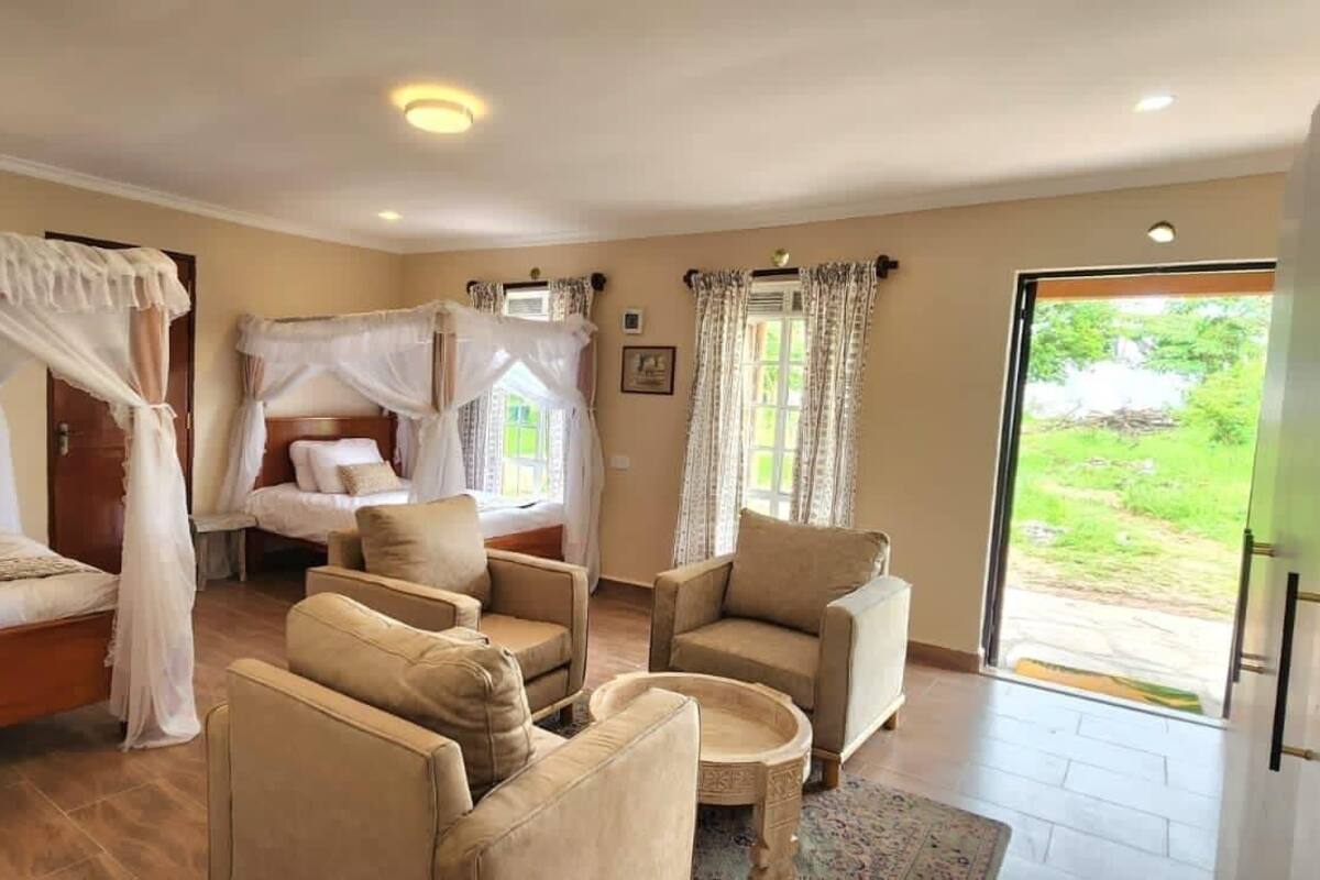 Een kamer met een bed, twee stoelen, een tafeltje en een raam met gordijnen.