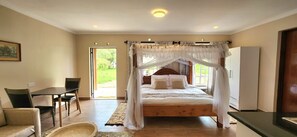A bedroom with a four-poster bed, a dining table, chairs, and a small seating area with a chair and a table. - Kileleoni Mara Gateway House - Adults Only (Maasai Mara)