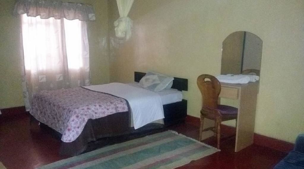 A bedroom with a bed, a chair, a desk, and a mirror.