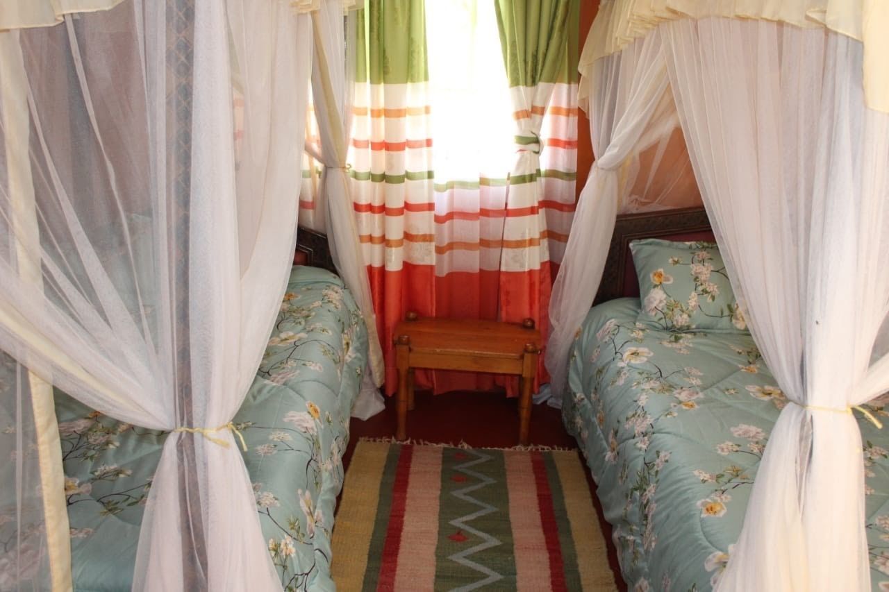 A room with two single beds, a bench, and a window with striped curtains.