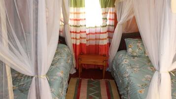A room with two single beds, a bench, and a window with striped curtains.