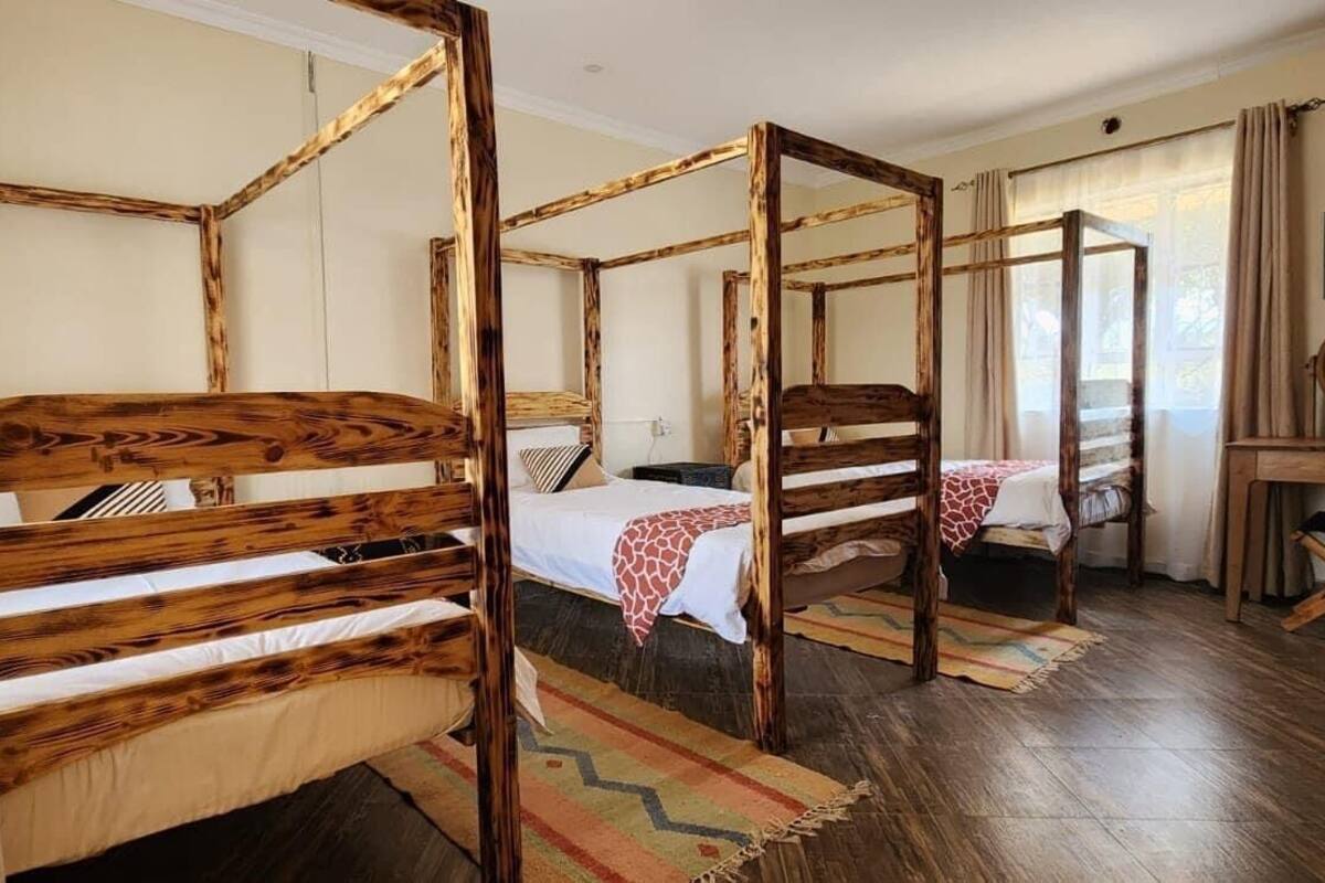 Een kamer met vier houten stapelbedden, een klein bureau met spiegel, en een raam met gordijnen.