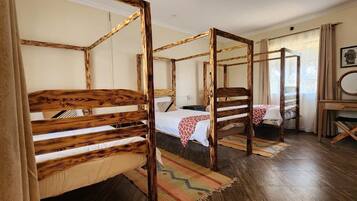 A room with four wooden bunk beds, a small desk with a mirror, and a window with curtains.