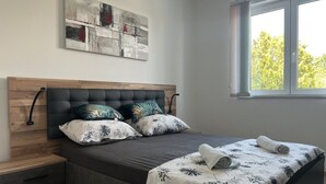 A bedroom with a wooden headboard, a bed with a floral bedspread, two pillows, a nightstand, and a window with a view of trees. - Apartment in Medulin with Terrace, Air condition, WIFI, Washing machine (4634-5) (Medulin)