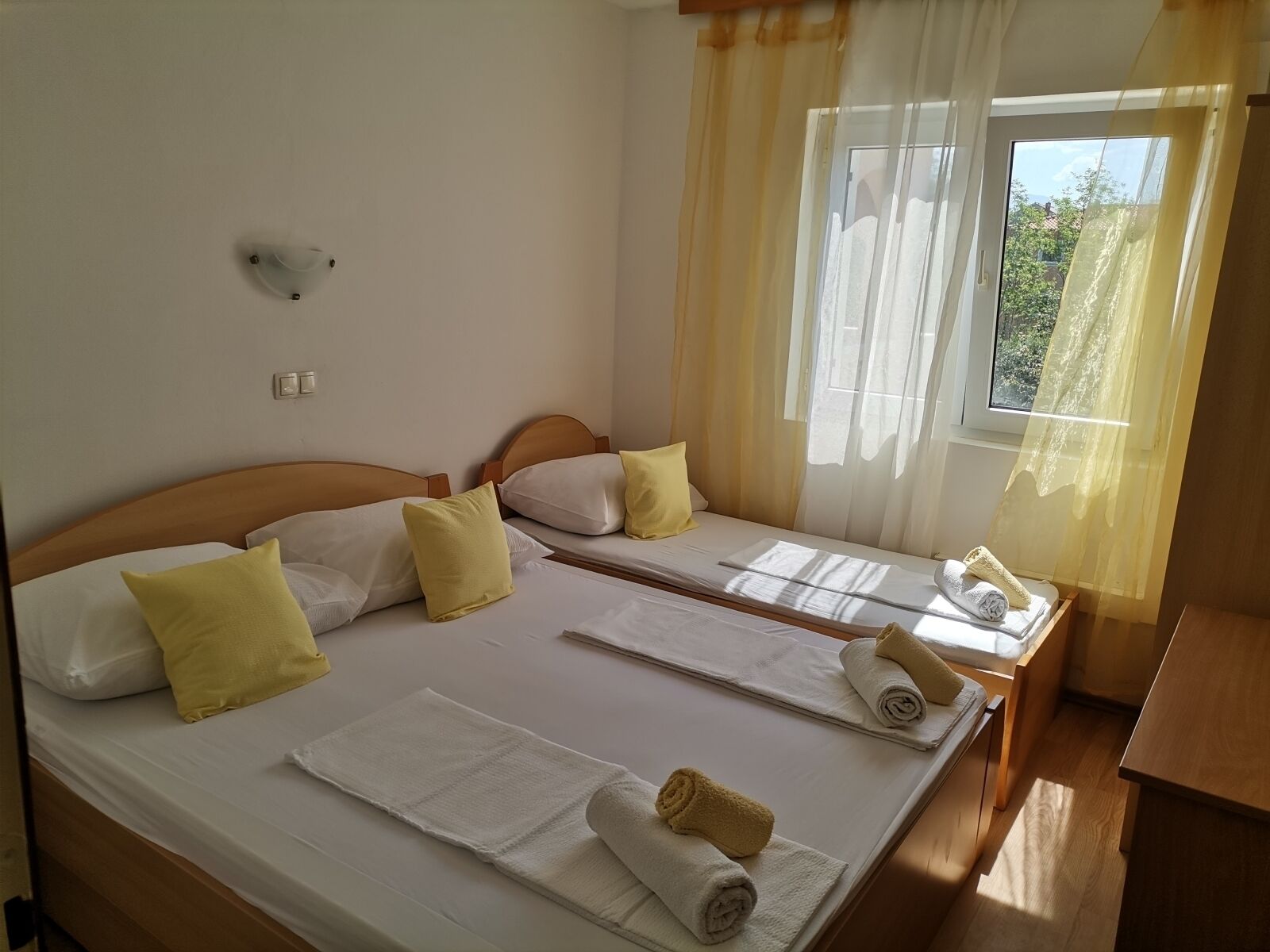 A hotel room with two beds, each with white linens, yellow pillows, and rolled towels.