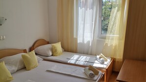 Une chambre d’hôtel avec deux lits, chacun agrémenté de draps blancs et d’oreillers jaunes, une tête de lit en bois, un bureau en bois et une fenêtre avec des rideaux légers.