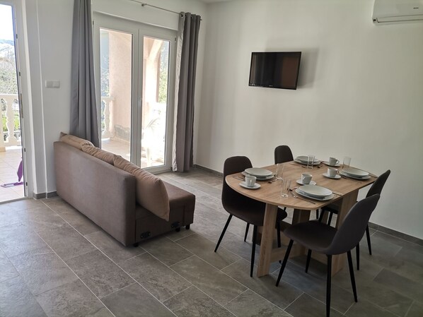 A dining area with a wooden table set for four, a sofa, and a TV mounted on the wall. - Apartment in Lopar with Terrace, Air condition, WIFI (4620-1) (Lopar)