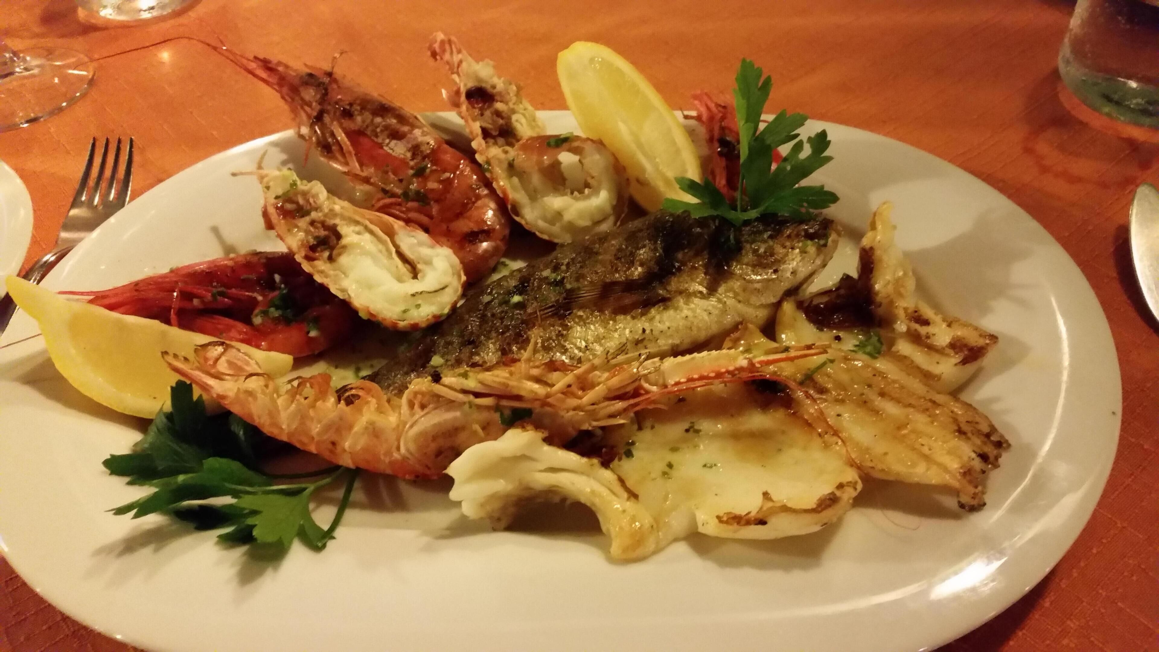 Un piatto di pesce, con pesce alla griglia, gamberi e, possibilmente, aragosta, guarnito con limone e prezzemolo.