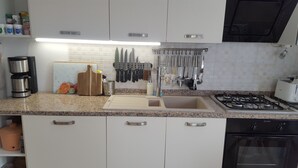 A kitchen with white cabinets, a granite countertop, a coffee maker, a cutting board, and various utensils hanging on the wall.
