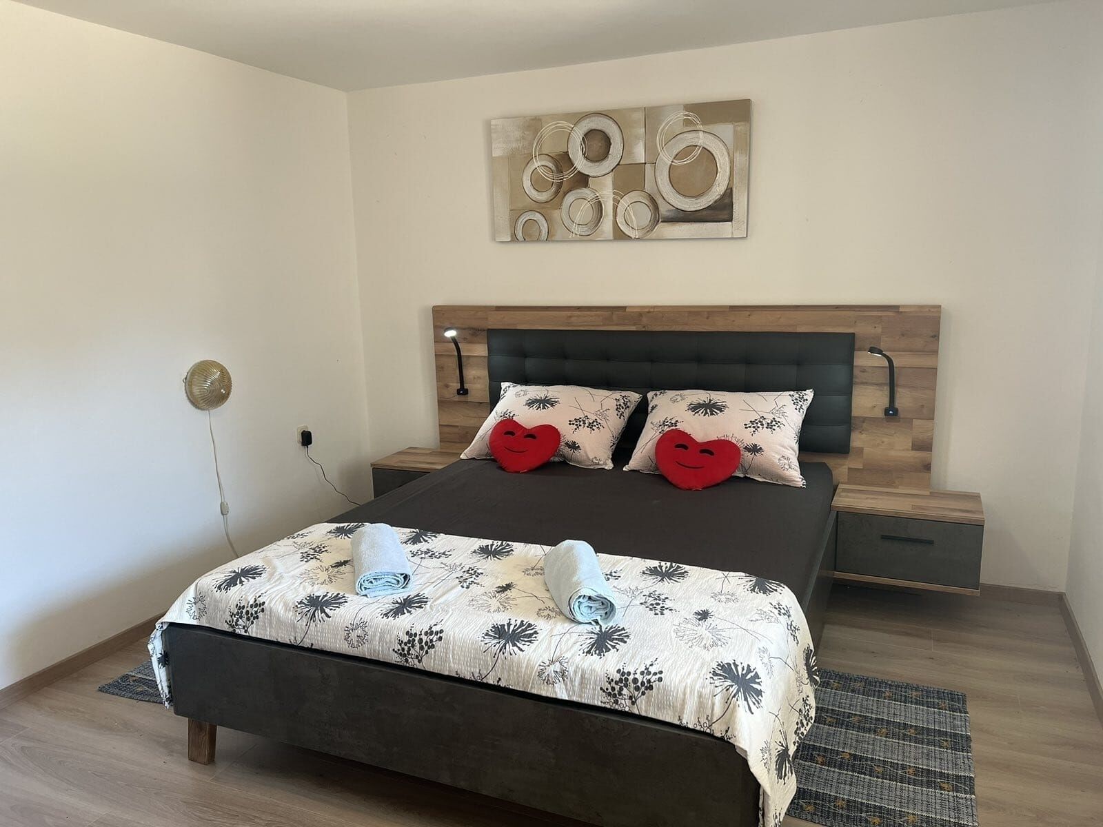 Ein modernes Schlafzimmer mit einem Holzkopfteil, zwei Nachttischen, einem Bett mit floralem Bettzeug und einem Wandbild über dem Bett.