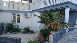 Ein modernes Gebäude mit Balkon, Klimaanlage und einem Garten mit verschiedenen Pflanzen und Blumen.