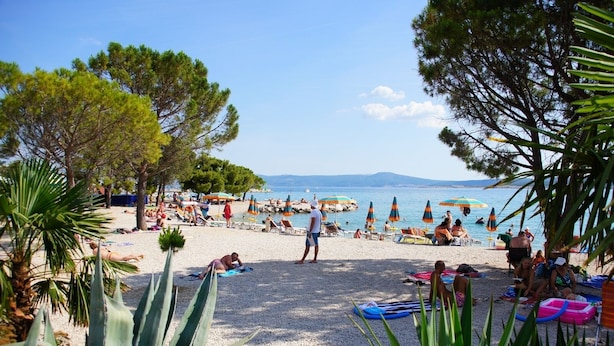 Una playa con gente tomando el sol, sombrillas y una vista despejada del mar.