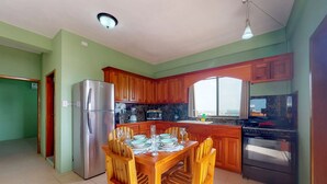 A kitchen with wooden cabinets, a stainless steel refrigerator, a stove, and a dining table set for six. - Laguna Hotel (San Pedro)